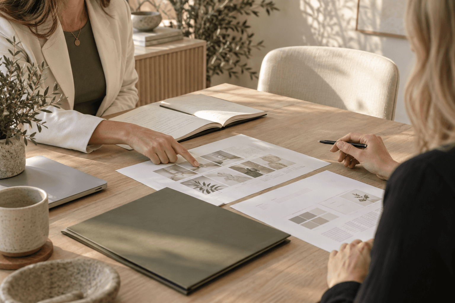 Hands reviewing a planning notebook and documents on a pale oak table.